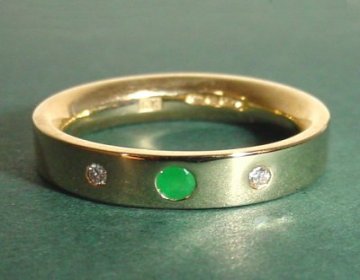 A 9ct yellow gold eternity ring with a central emerald flanked by 2 SI quality diamonds.