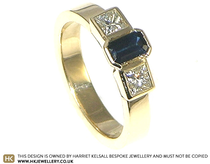 Bespoke 9ct yellow gold engagement ring with 0.35ct emrald cut dark blue 4.9x3mm sapphire with two 3mm princess cut H SI diamonds totaling 0.33cts.